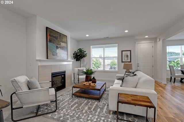 living room featuring a wealth of natural light, a tiled fireplace, and wood-type flooring