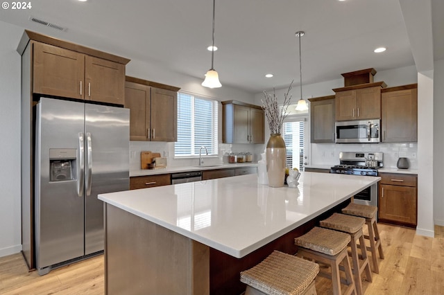 kitchen with hanging light fixtures, appliances with stainless steel finishes, light hardwood / wood-style floors, sink, and a kitchen island