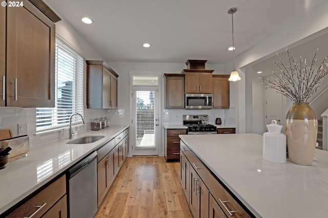 kitchen with light hardwood / wood-style flooring, decorative light fixtures, stainless steel appliances, sink, and tasteful backsplash