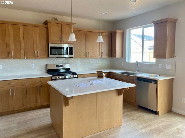 kitchen with light countertops, appliances with stainless steel finishes, a kitchen island, and a sink