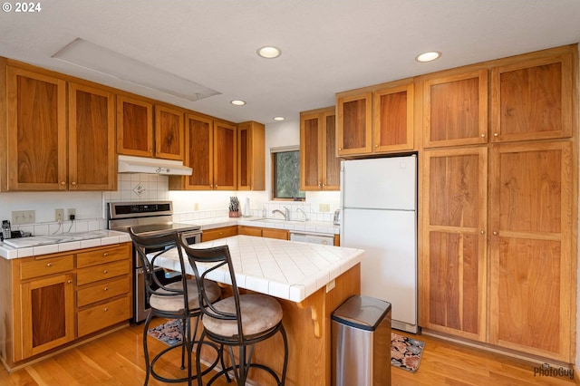 kitchen with white appliances, tile counters, a kitchen island, and light wood-type flooring