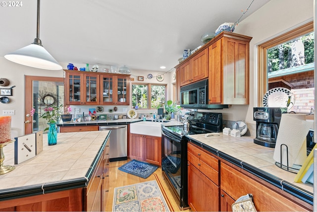 kitchen featuring decorative light fixtures, tile counters, light wood-type flooring, and black appliances