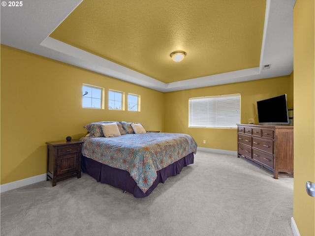 bedroom featuring a raised ceiling, light colored carpet, and a textured ceiling