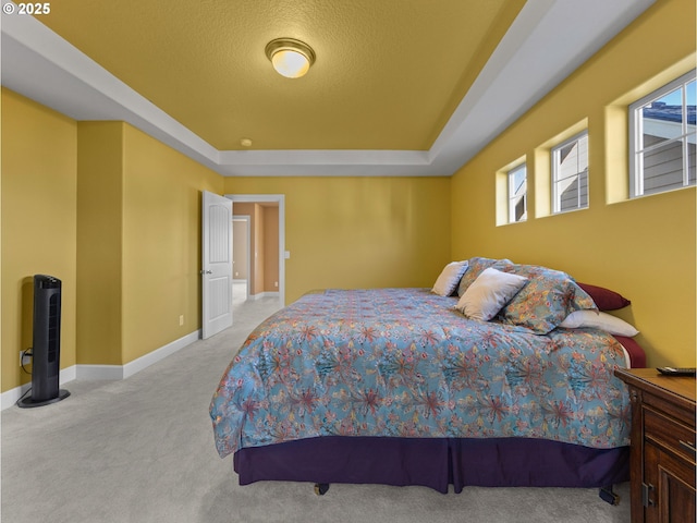 bedroom featuring light carpet, a textured ceiling, and a tray ceiling