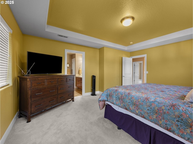 carpeted bedroom with a tray ceiling, ensuite bath, and a textured ceiling