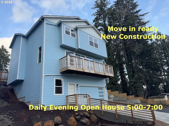 rear view of house featuring a garage, board and batten siding, a balcony, and fence