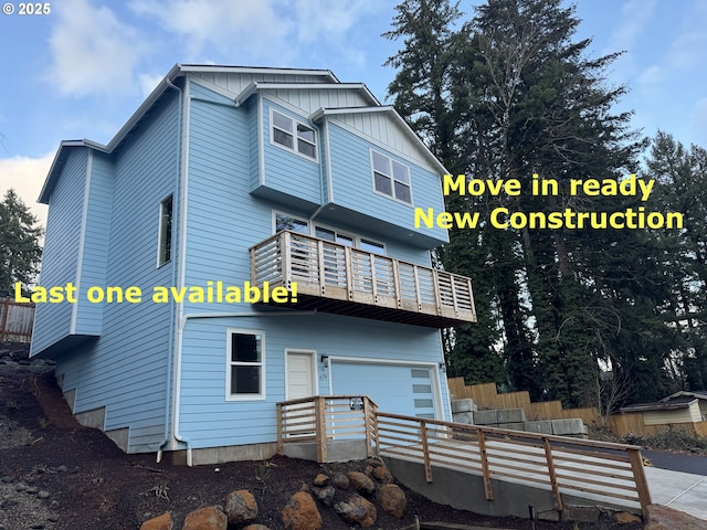 rear view of property with board and batten siding, an attached garage, a balcony, and fence