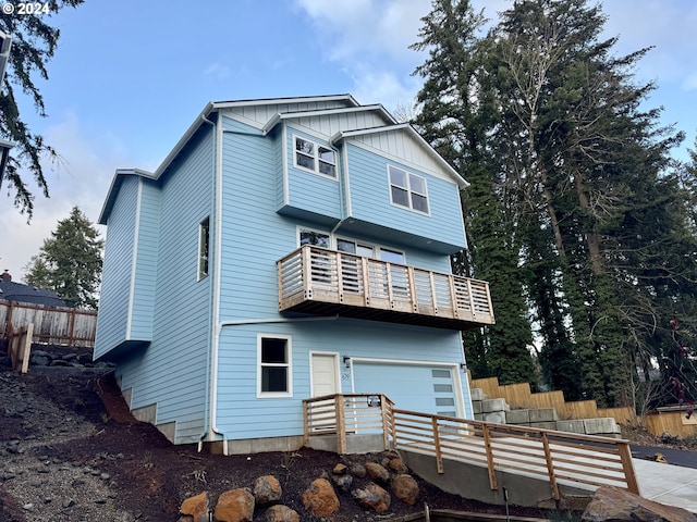 back of house featuring board and batten siding, an attached garage, fence, and a balcony