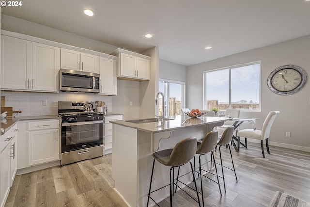 kitchen featuring sink, appliances with stainless steel finishes, white cabinets, a center island with sink, and decorative backsplash