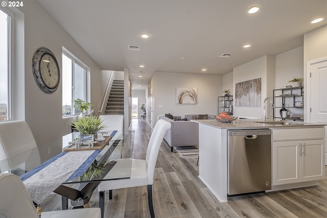 kitchen featuring sink, white cabinetry, light hardwood / wood-style flooring, stainless steel dishwasher, and a kitchen island with sink