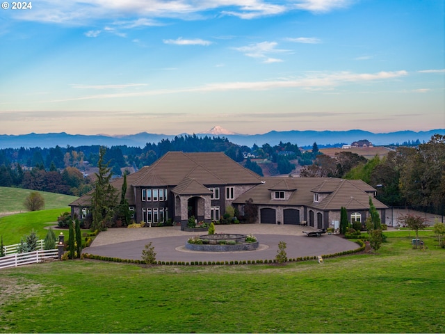 rear view of house featuring curved driveway, stone siding, a mountain view, and a tile roof