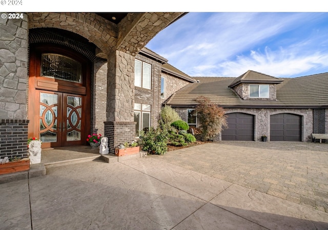 property entrance featuring brick siding, french doors, decorative driveway, and an attached garage
