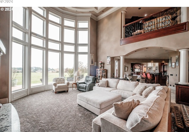 carpeted living room featuring a towering ceiling, decorative columns, crown molding, and arched walkways