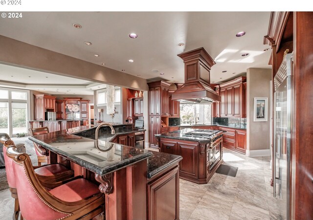 kitchen featuring a large island with sink, recessed lighting, dark stone counters, a breakfast bar, and a sink