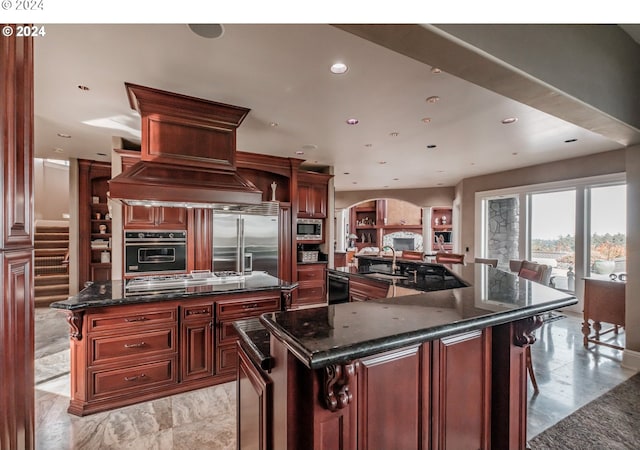 kitchen featuring a spacious island, built in appliances, a kitchen bar, and dark stone counters