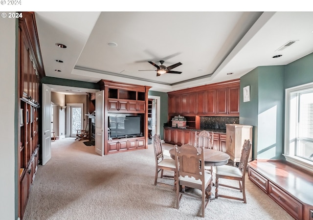 dining area with ceiling fan, light carpet, and a tray ceiling