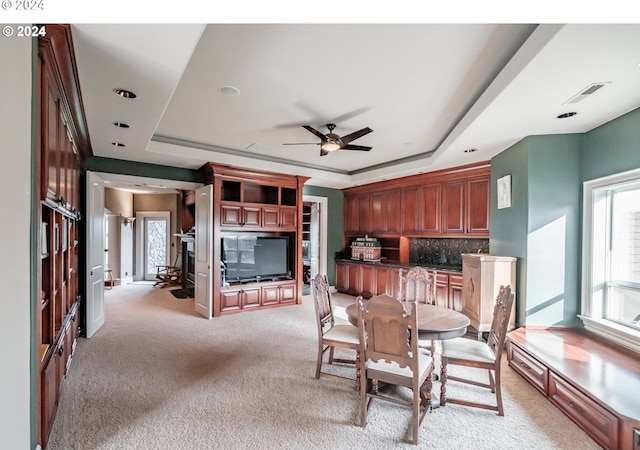 dining area featuring a tray ceiling, light carpet, and a ceiling fan