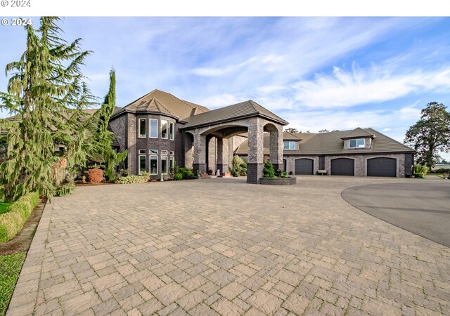 french country style house with curved driveway, brick siding, and an attached garage