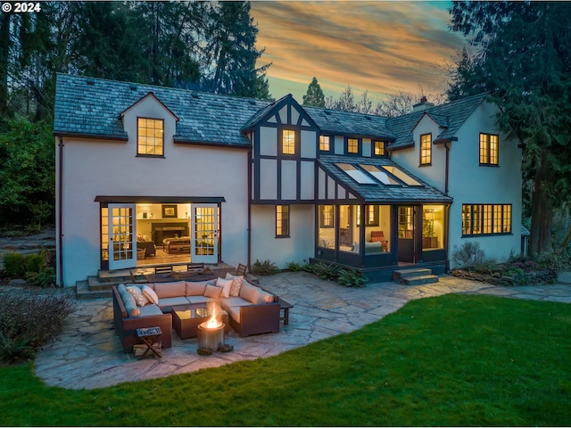 back house at dusk with a patio area, outdoor lounge area, and a lawn