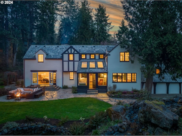 back house at dusk featuring a patio area, an outdoor living space, and a lawn