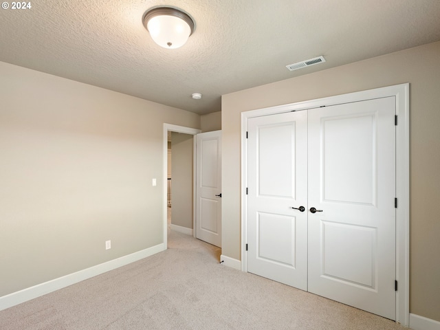 unfurnished bedroom with a textured ceiling, light carpet, and a closet