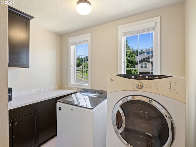 laundry area featuring a textured ceiling, cabinets, washing machine and clothes dryer, and plenty of natural light