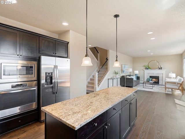 kitchen featuring light stone counters, pendant lighting, a kitchen island, dark wood-type flooring, and stainless steel appliances