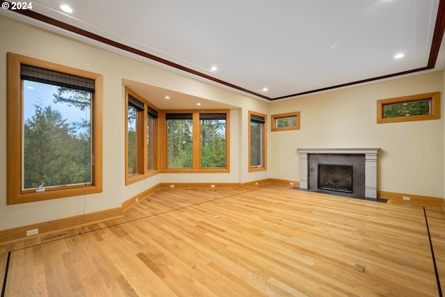 unfurnished living room featuring light wood-type flooring, ornamental molding, a premium fireplace, and a wealth of natural light