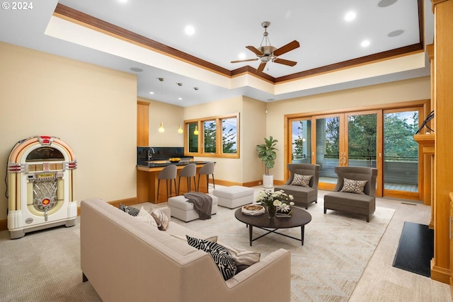 living room featuring ornamental molding, light colored carpet, ceiling fan, and a raised ceiling