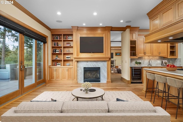 living room with light wood-type flooring, ornamental molding, sink, and wine cooler