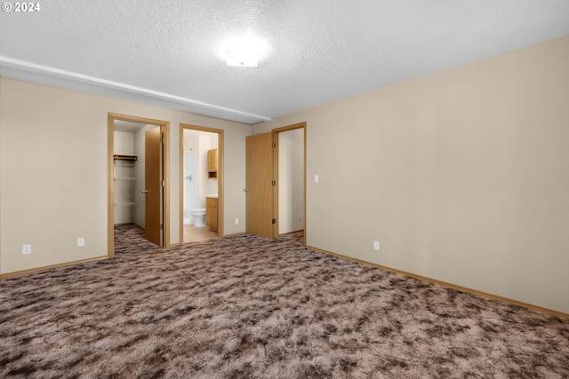 unfurnished bedroom with ensuite bathroom, carpet floors, a textured ceiling, a walk in closet, and a closet