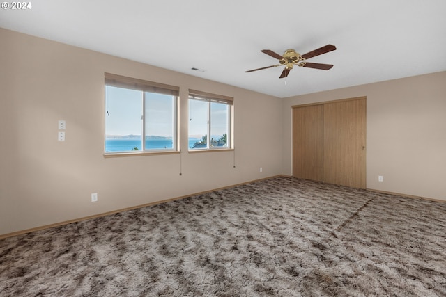 unfurnished bedroom featuring ceiling fan, a water view, carpet floors, and a closet