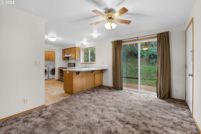 kitchen featuring kitchen peninsula, a kitchen bar, stainless steel electric stove, ceiling fan, and washer and dryer