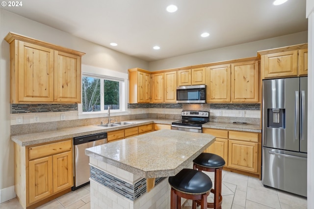 kitchen featuring light tile patterned flooring, a kitchen island, appliances with stainless steel finishes, sink, and a kitchen bar