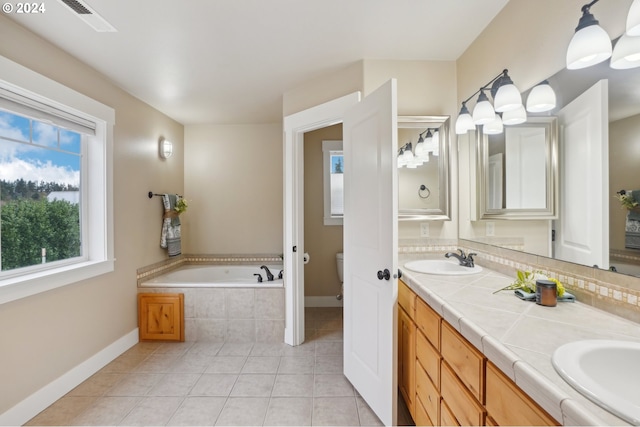 bathroom featuring tile patterned flooring, vanity, tiled bath, and toilet