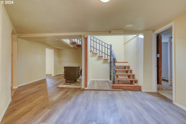 basement featuring a wood stove, light hardwood / wood-style flooring, and a textured ceiling