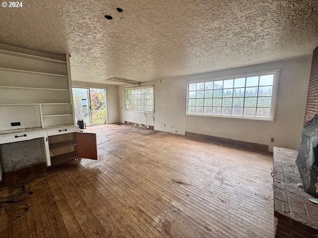 unfurnished living room featuring plenty of natural light, wood-type flooring, and a textured ceiling