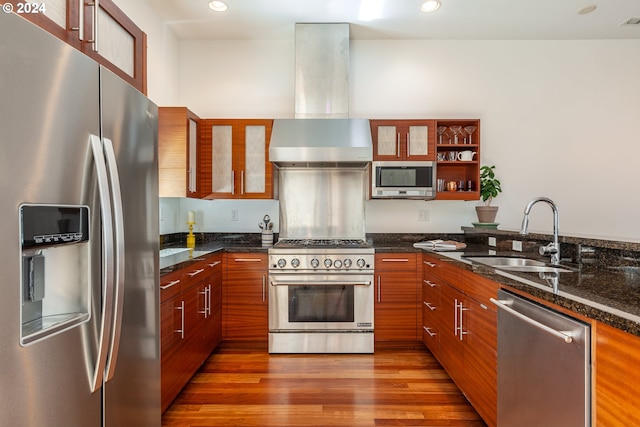 kitchen with extractor fan, sink, dark stone counters, stainless steel appliances, and hardwood / wood-style floors