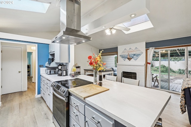 kitchen featuring white cabinetry, stainless steel appliances, light hardwood / wood-style flooring, island exhaust hood, and vaulted ceiling with skylight