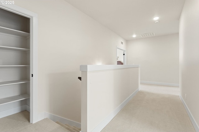 corridor with carpet flooring, an upstairs landing, visible vents, and baseboards