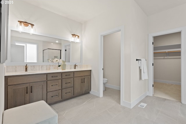 bathroom with a shower stall, double vanity, a sink, and toilet
