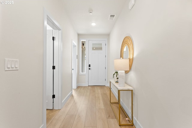 hallway featuring light wood finished floors, baseboards, and visible vents