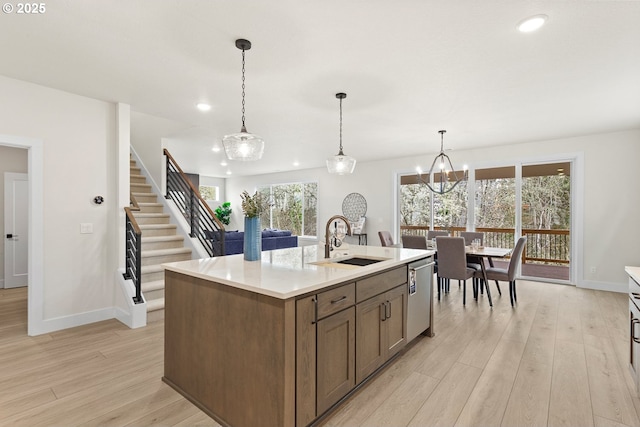 kitchen featuring an island with sink, dishwasher, a sink, light countertops, and light wood finished floors