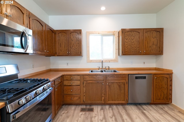 kitchen featuring a sink, light wood-style floors, light countertops, appliances with stainless steel finishes, and brown cabinets