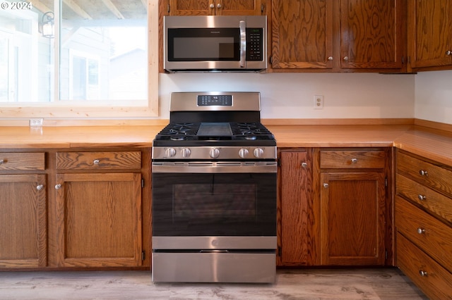 kitchen featuring appliances with stainless steel finishes, brown cabinetry, light wood-type flooring, and wood counters