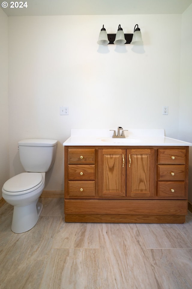 half bath featuring baseboards, vanity, and toilet