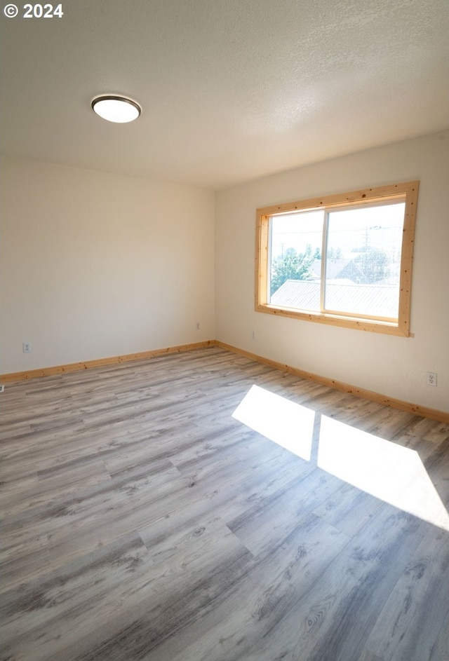 unfurnished room featuring a textured ceiling, light wood-style flooring, and baseboards