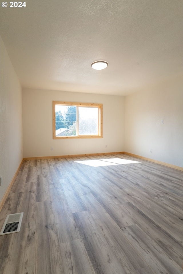 spare room with a textured ceiling, wood finished floors, visible vents, and baseboards