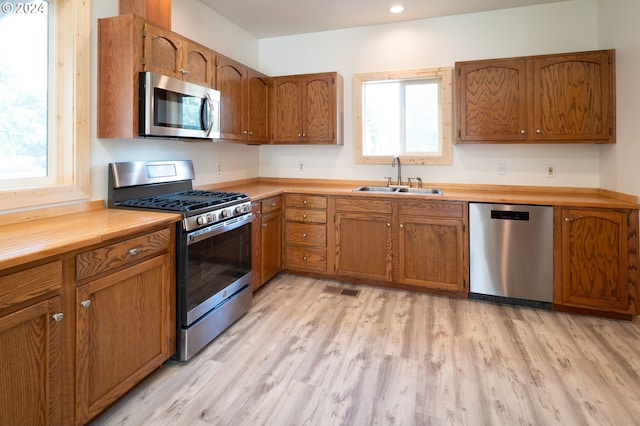 kitchen with a sink, stainless steel appliances, brown cabinetry, and light countertops