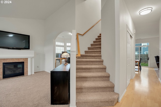 stairs featuring a tiled fireplace, plenty of natural light, a towering ceiling, and wood-type flooring